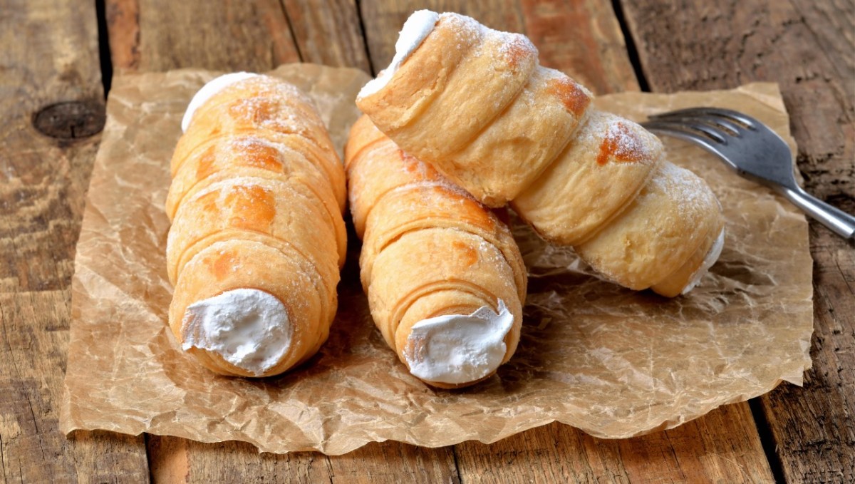 Drei Schaumrollen mit Vanillecreme auf einem Stück Backpapier.