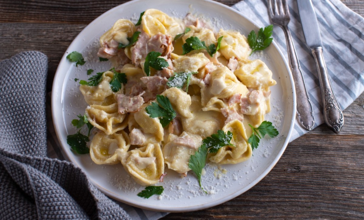 Eine Portion Tortellini alla panna auf einem weiÃŸen Teller. Besteck liegt daneben.