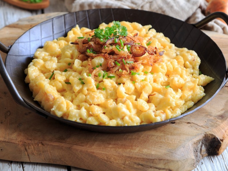 Eine gusseiserne Pfanne vegane Käsespätzle mit Röstzwiebeln und Petersilie, Nahaufnahme.