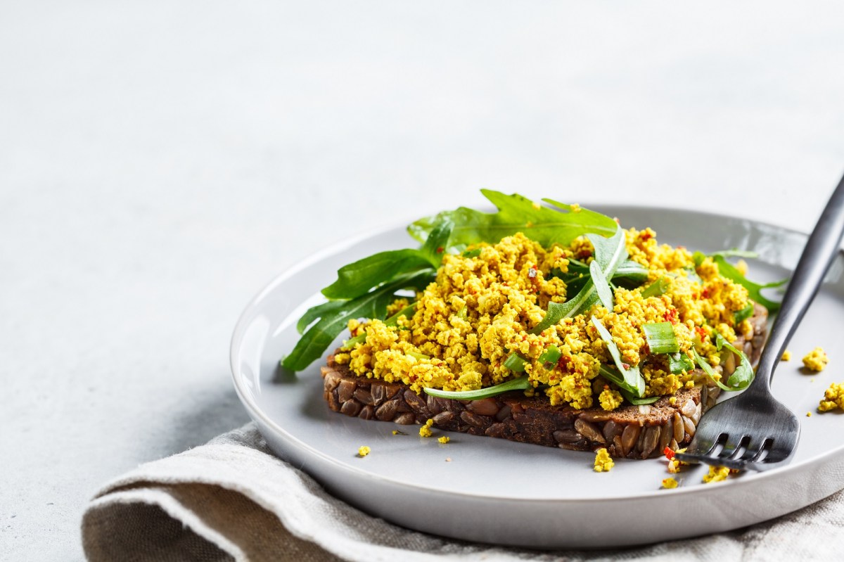 Ein Brot belegt mit veganem Rührei und Rucola auf einem Teller, Nahaufnahme.