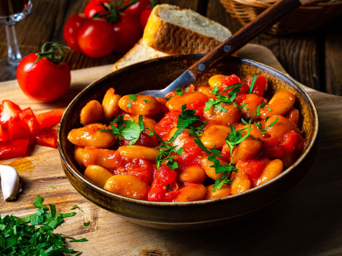 WeiÃŸe Bohnen-Pfanne, serviert in einer Pfanne. Tomaten und andere KrÃ¤uter liegen als Dekoration daneben.