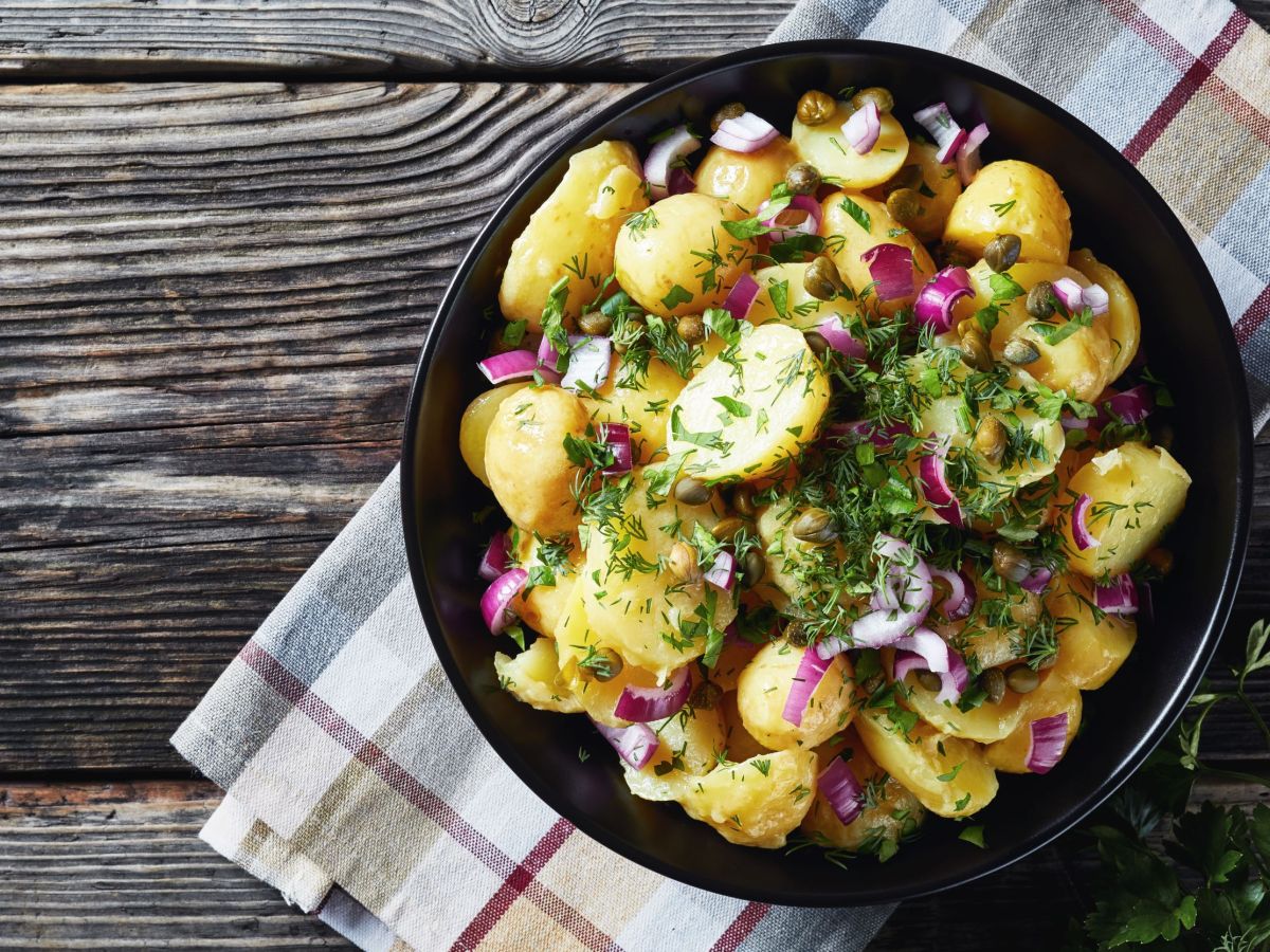 Winterlicher Kartoffelsalat in einer Schüssel steht auf einem karierten Handtuch.