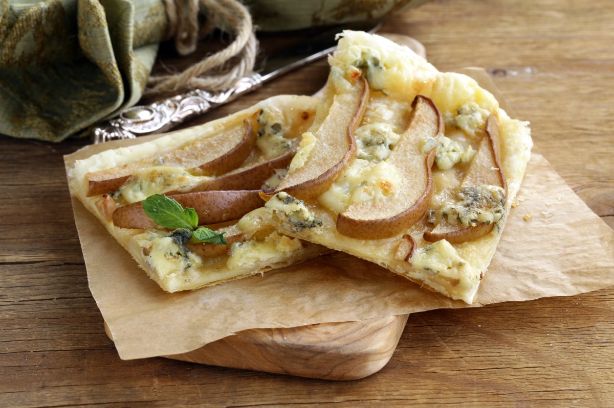 Zwei Stücke Blätterteig-Tarte mit Birne und Blauschimmelkäse auf Backpapier und einem Holzbrett.