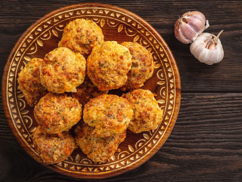 Blumenkohl-Mozzarella-Bällchen, arrangiert auf einem orientalischen Teller. Daneben liegen zwei Knoblauchknollen als Deko.