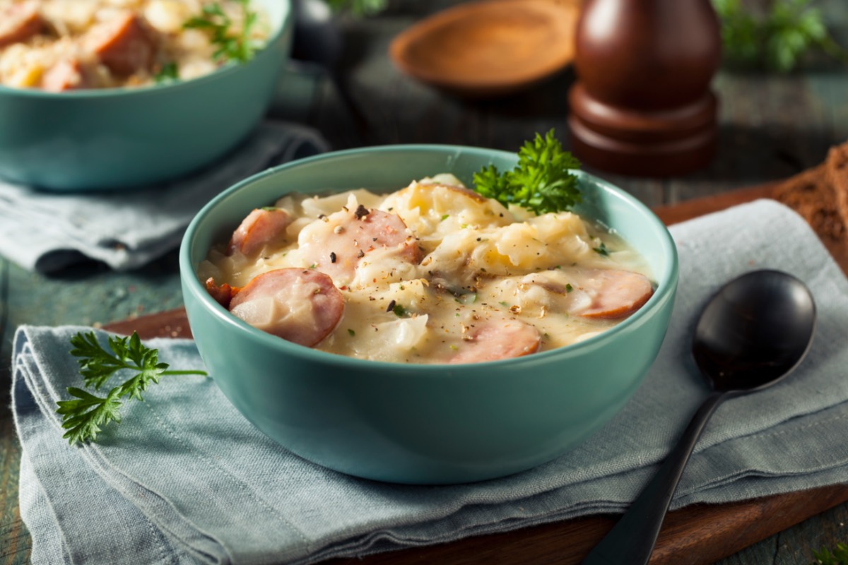 Eine Schüssel cremige Sauerkrautsuppe mit Würstchen und Petersilie.