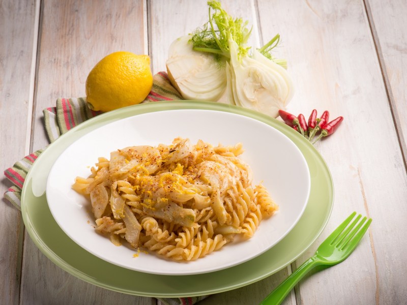 Ein Teller mit Nudeln und Fenchel auf grünem Tuch und hellem Untergrund