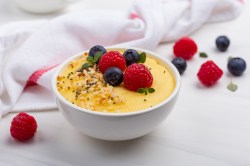 Eine weiße Schüssel Frühstücks-Polenta mit Nüssen und Beeren, drumherum ein Geschirrtuch und frische Beeren.