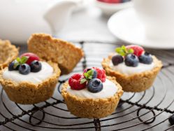 Vier Granola Cups mit Beeren und Joghurt stehen auf einem Kuchengitter.