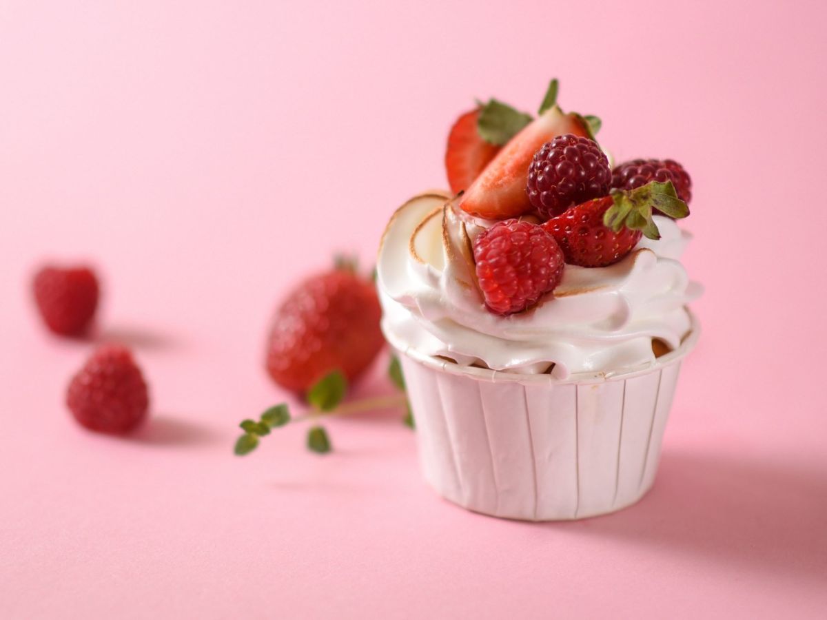 Himbeer-Baiser-Creme in einem kleinen Förmchen. Daneben liegen frische Früchte als Dekoration.