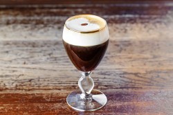 Ein Glas Irish Coffee auf einem Holztisch, garniert mit einerKaffeebohne.