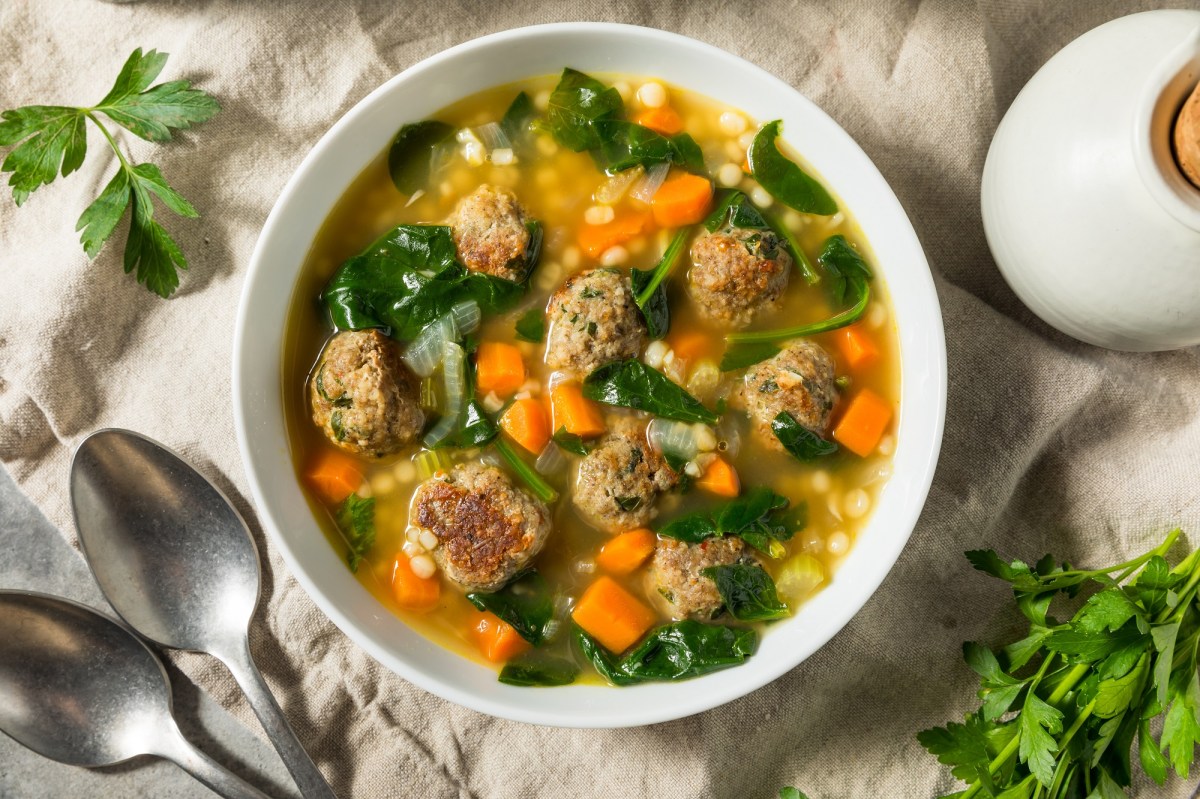 Eine Schale mit einer klaren Suppe und Einlage aus Hackbällchen, Möhren und kleinen Nudeln auf hellem Untergrund