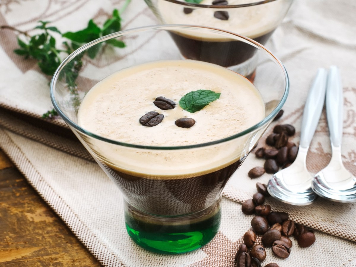 Kaffee-Zitronen-Shake in einem klassischen Glas, garniert mit Minze und Kaffeebohnen. Daneben zwei LÃ¶ffel und noch mehr Kaffeebohnen.