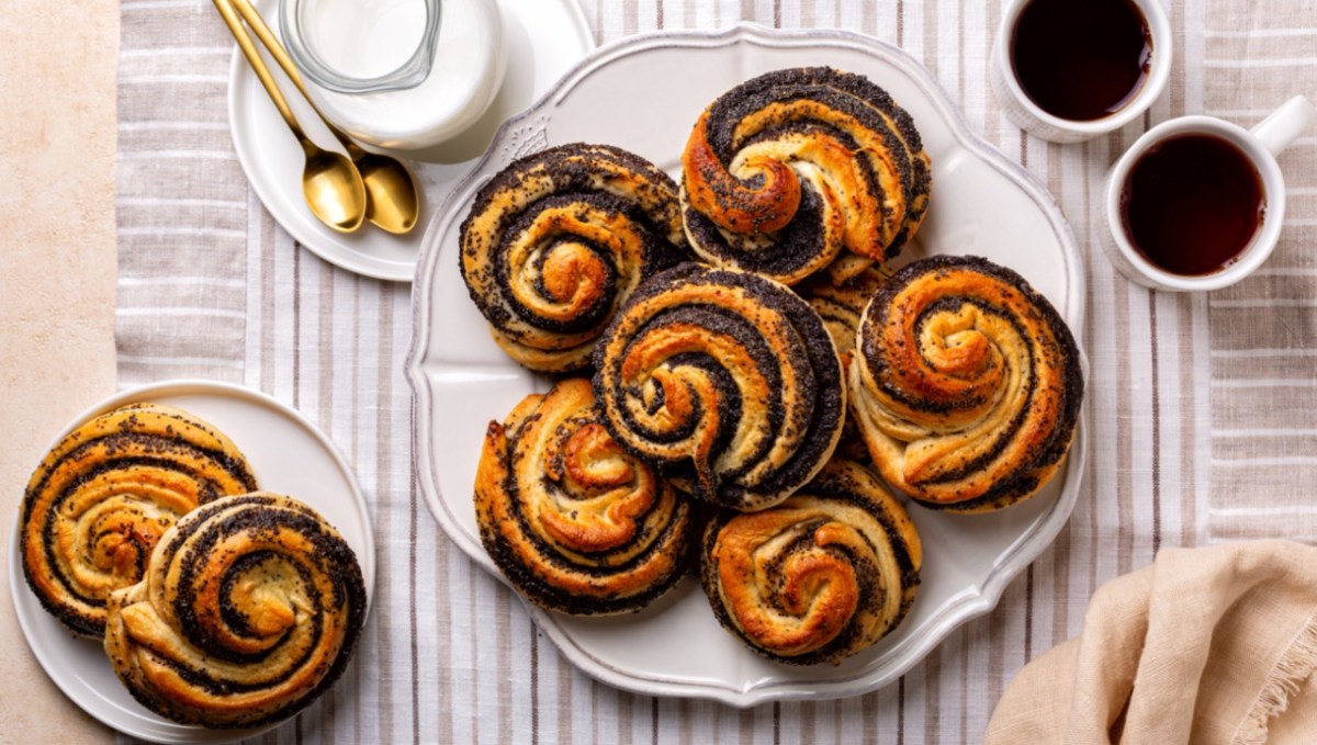 Ein Teller voller Mohnschnecken, von oben fotografiert. Daneben stehen zwei Tassen Kaffee und ein weiterer Teller mit Mohnschnecken. Außerdem ein Kännchen Milch.