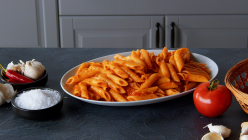 Penne Arrabiata, angerichtet auf einem Teller. Tomaten und Gewürze liegen außen herum.