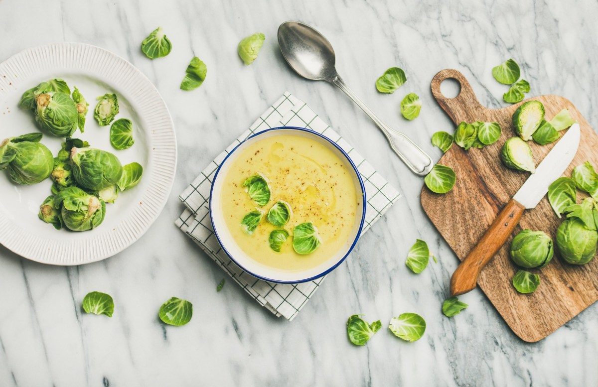 Eine Schüssel cremige Rosenkohlsuppe mit Schneidebrett, Messer, Rosenkohl und Löffel.