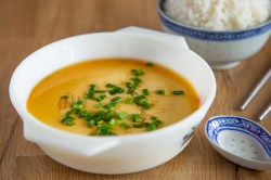 Steamed Eggs in einer Porzellanschale, garniert mit Schnittlauch und Sojoasoße. Daneben eine Schale Reis.