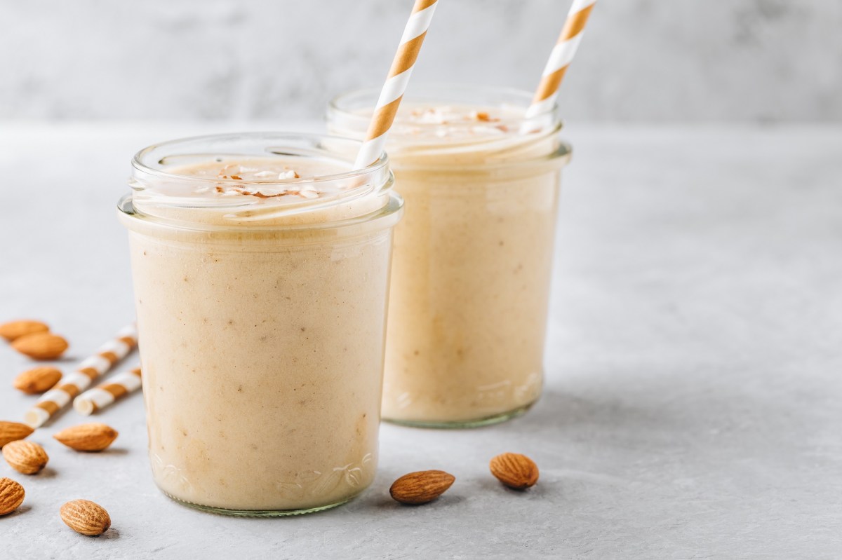 zwei Gläser mit Vanille-Mandel-Smoothie mit Strohhalm und Mandeln auf grauem Untergrund