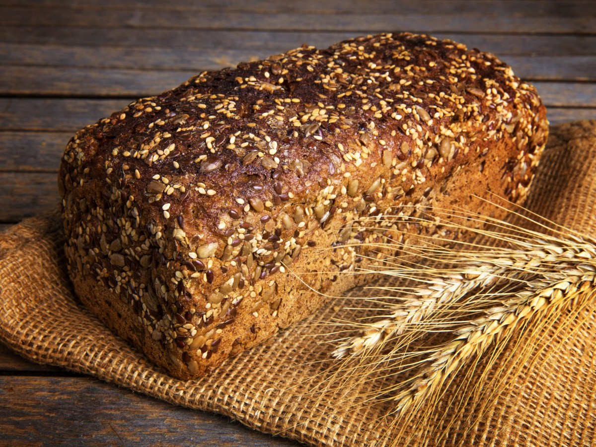 Ein Laib Vollkornbrot mit verschiedenen Saaten auf einem Mehlsack. Daneben zwei GetreideÃ¤hren.