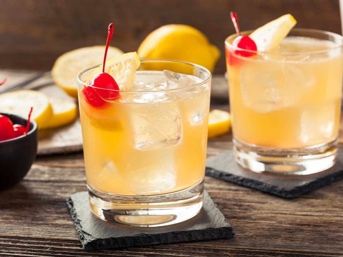 zwei GlÃ¤ser Whiskey Sour auf Eis mit Cocktailkirschen garniert.