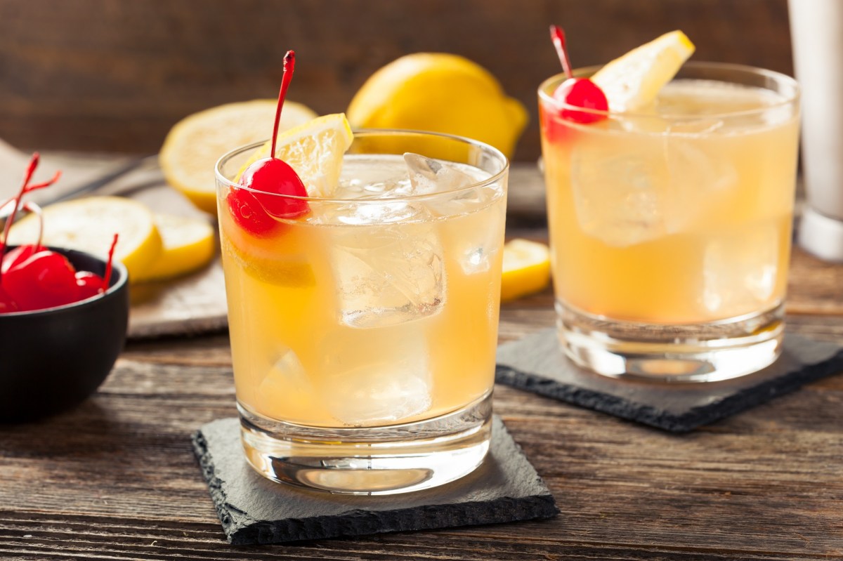 zwei Gläser Whiskey Sour auf Eis mit Cocktailkirschen garniert.