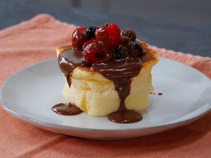 Ein fluffiger Würfelkuchen mit Schokosoße und frischen Beeren auf einem Teller.