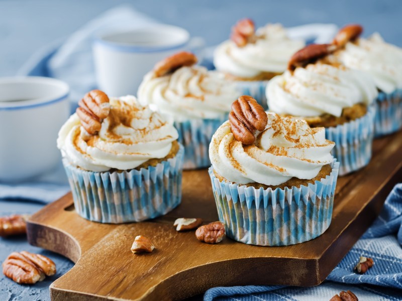 Mehrere Zimtschnecken-Cupcakes mit Zimt und Pekannüssen verziert, sie stehen auf einem Brett.