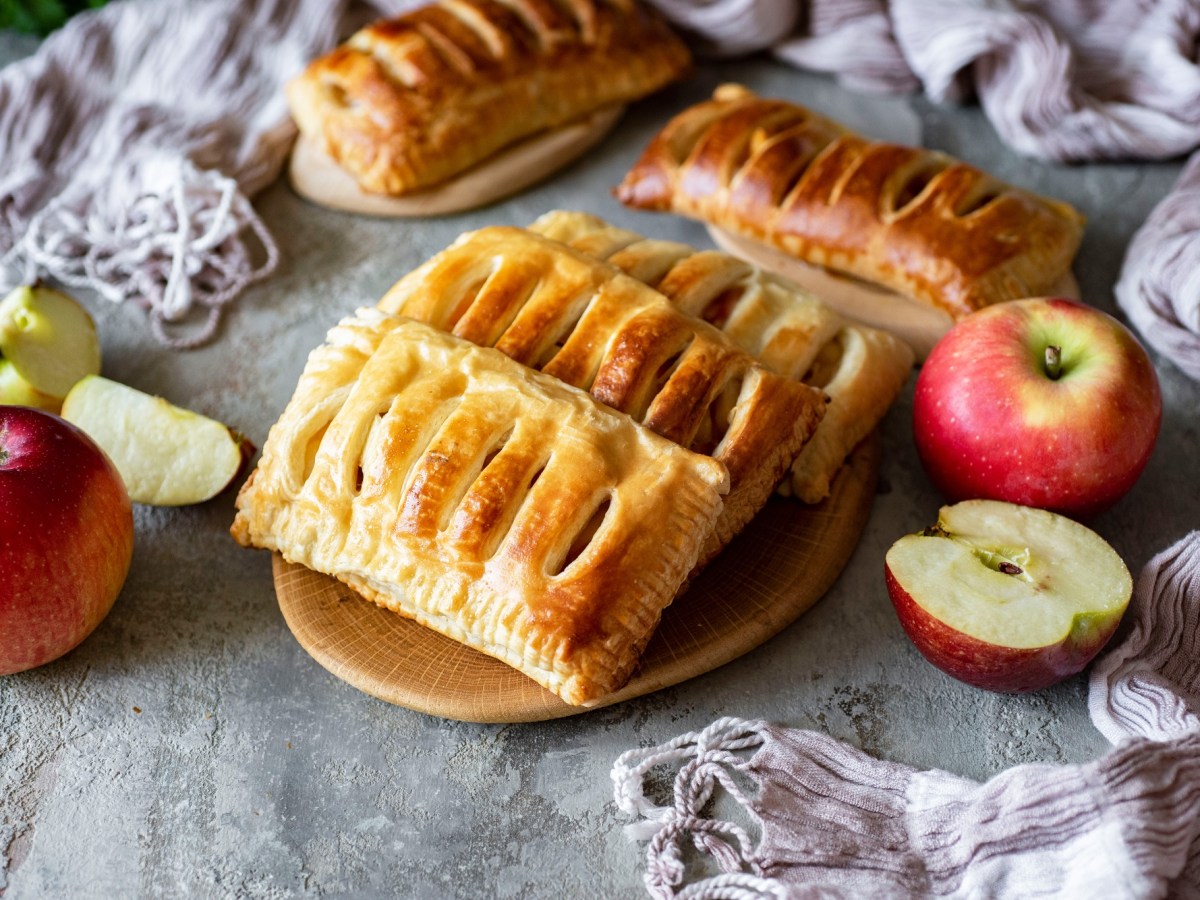 4 Apfel-Quark-Taschen auf einem Teller, drumherum ganze und halbierte Ã„pfel.