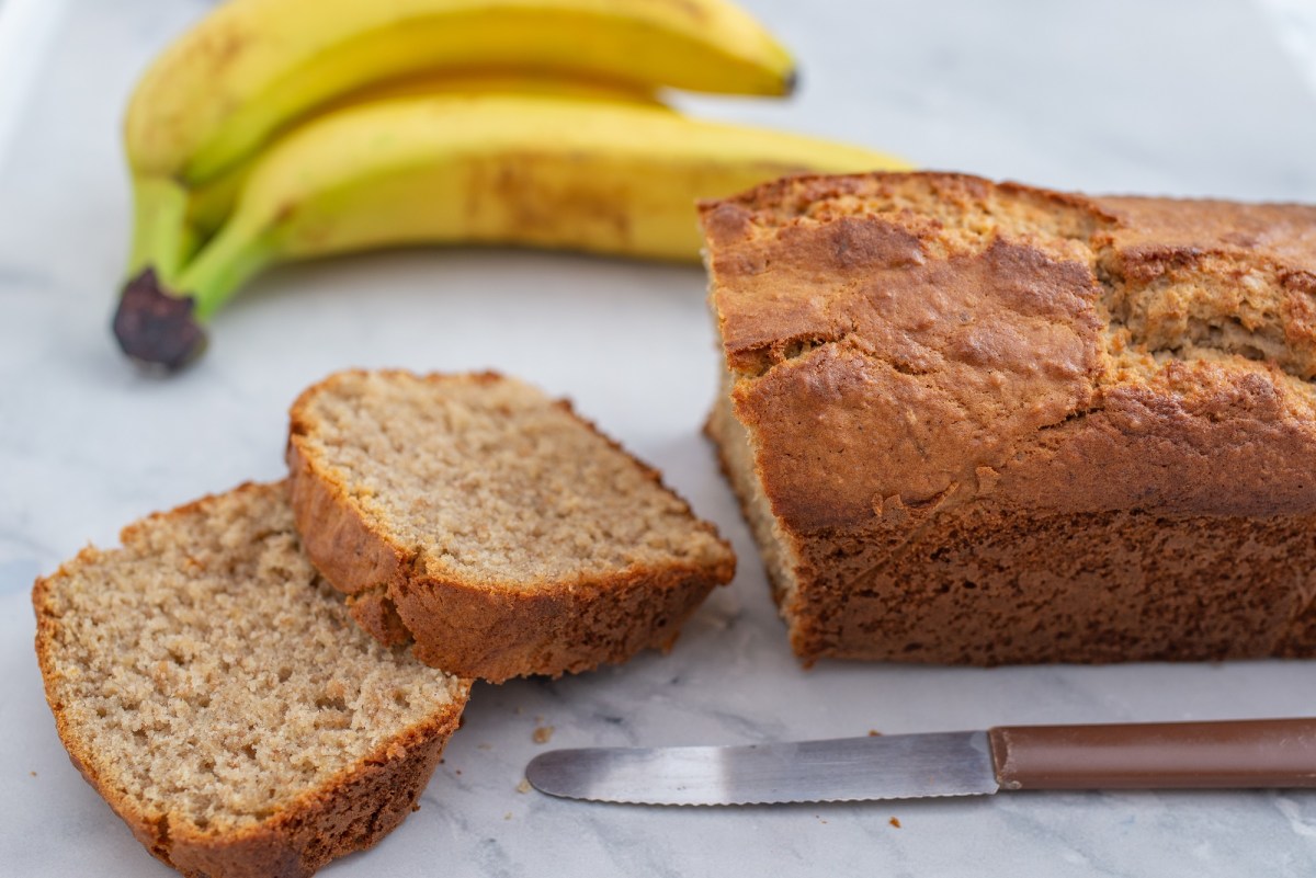 Angeschnittenes Bananenbrot ohne Ei, davor ein Messer, dahinter zwei Bananen.