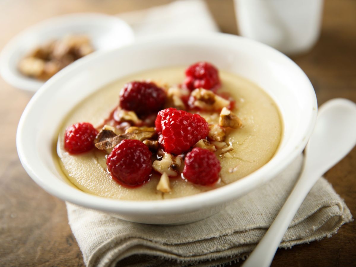 Grießpudding-Bowl in einer Schüssel angerichtet, dekoriert mit frischen Beeren und Nüssen. Die Schale steht auf einer hellen Stoffserviette und ein weißer Teelöffel liegt daneben.