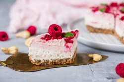 Ein Stück Himbeer-Cheesecake auf einem Tortenheber, garniert mit Himbeeren und Fruchtsoße, im Hintergrund der angeschnittene Kuchen.