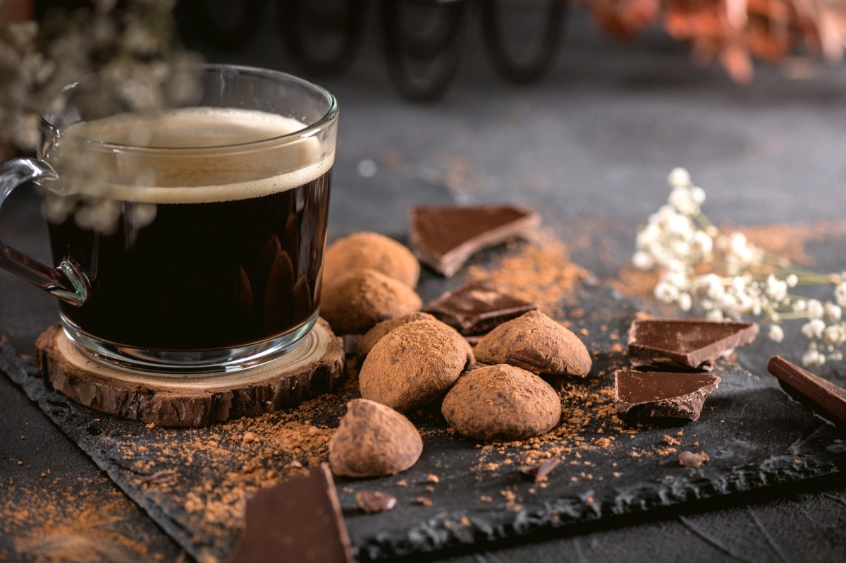 Schieferplatte mit Schokoladenstücken und Kaffee-Pralinen und einem Glas schwarzen Kaffee.