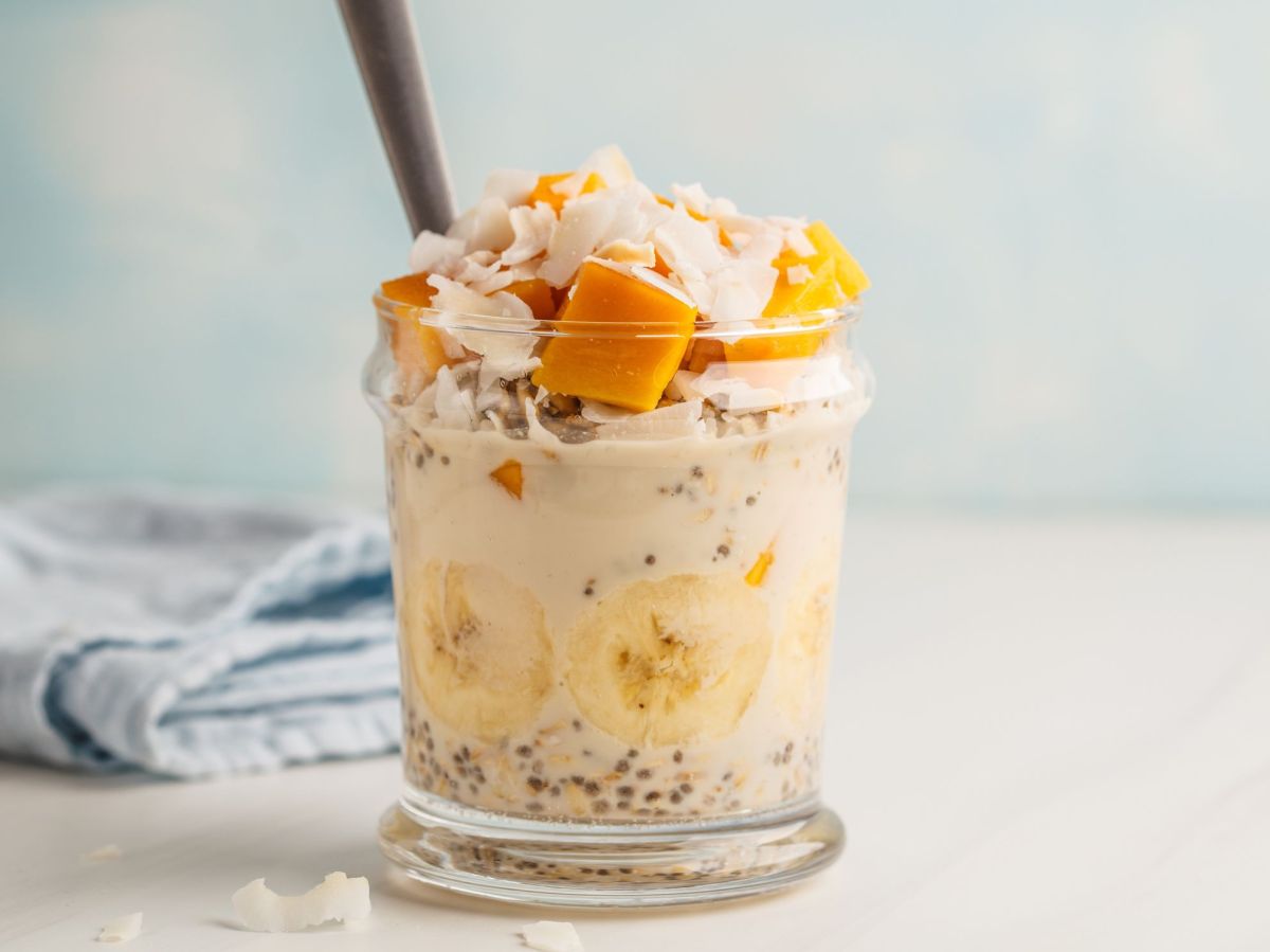 Mango Kokos Overnight Oats im Glas geschichtet und serviert mit einem Strohhalm.