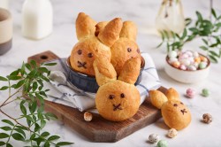 ein paar Osterhasen-Brötchen auf einem Brett miteinem Geschirrtuch, drumherum Osterdeko und Zweige.