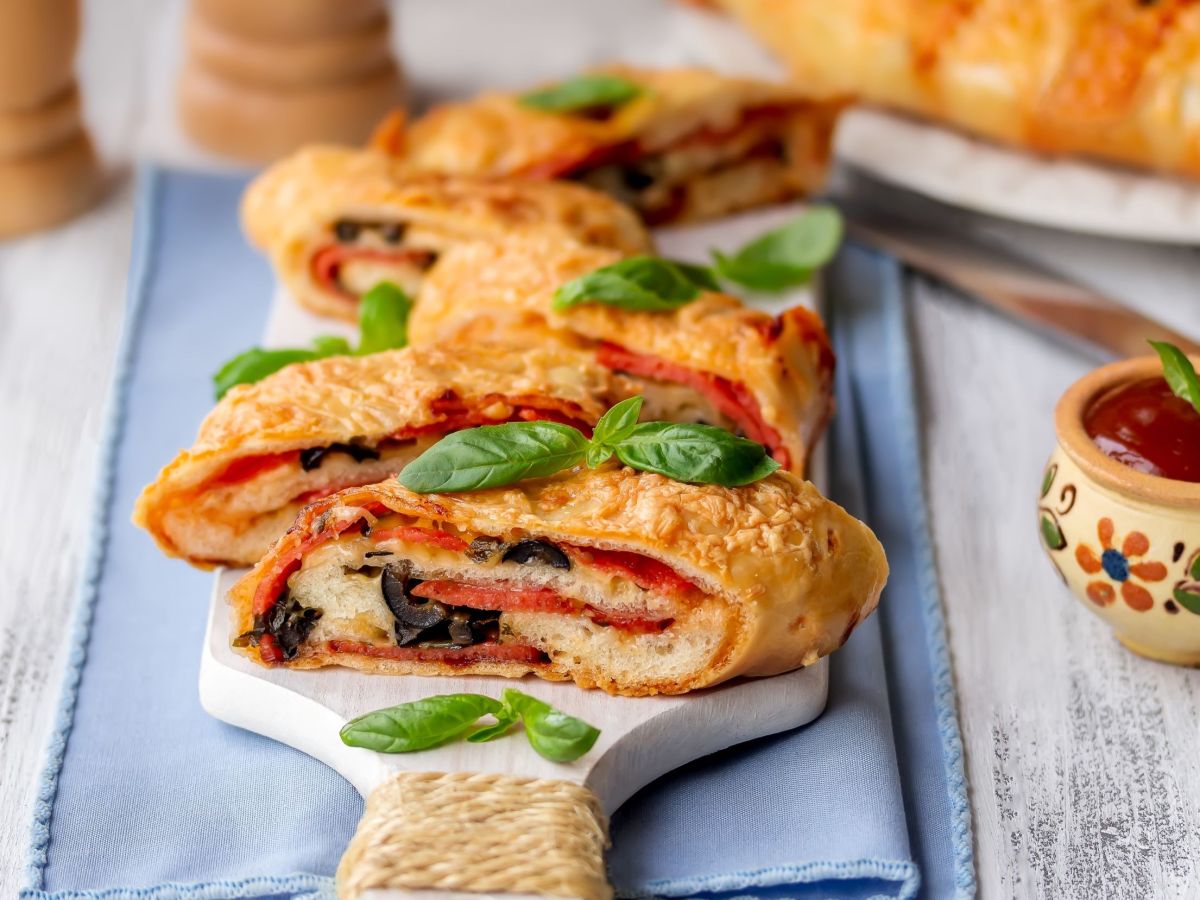 Pesto-Strudel auf einem Holzbrett angerichtet, darunter liegt ein blaues Handtuch.