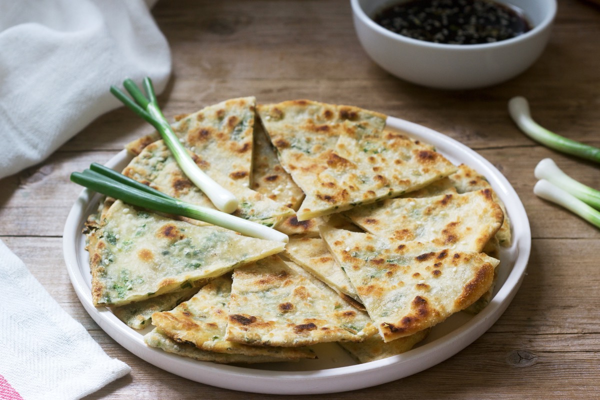 Mehrere in StÃ¼cke geschnittene Pfannkuchen mit FrÃ¼hlingszwiebeln auf einem Teller. Obendrauf liegen ein paar Lauchzwiebeln.