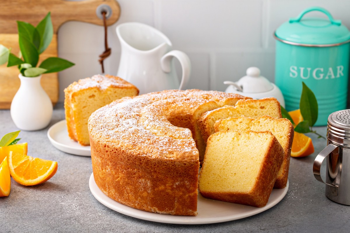 Ein angeschnittener Pfundkuchen auf einer hellgrauen Arbeitsfläche. Daneben stehen eine Zuckerdose, ein Krug und ein Puderzucker-Streuer.