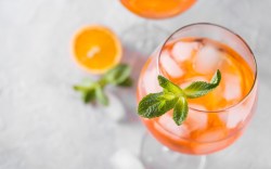 Ein Glas Rhabarber Spritz mit Minze von oben fotografiert. Daneben liegen eine Orangenscheibe und Minzblätter.