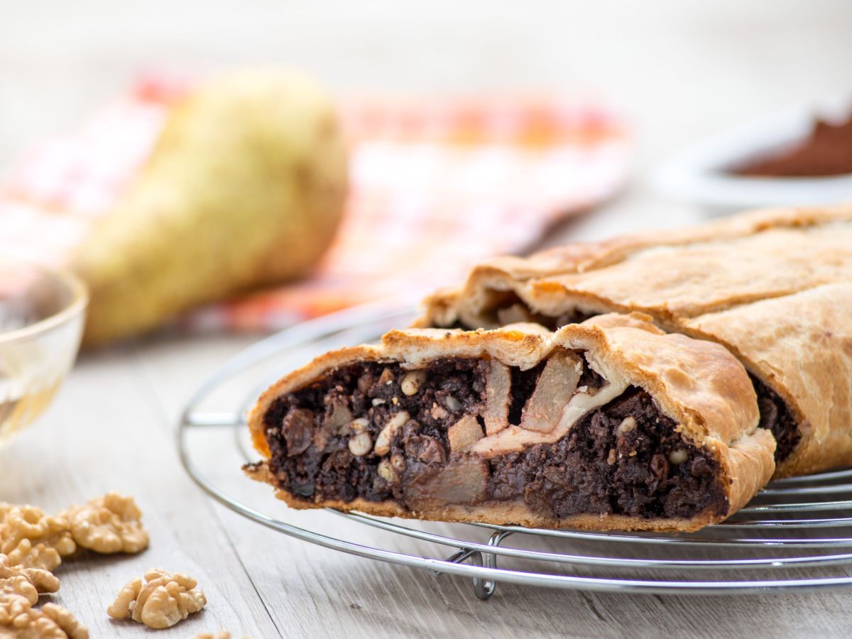 Schoko-Birnen-Strudel, in Scheiben geschnitten auf einem Gitter liegend. Im Hintergrund und daneben liegen eine Birne und WalnÃ¼sse als Deko.