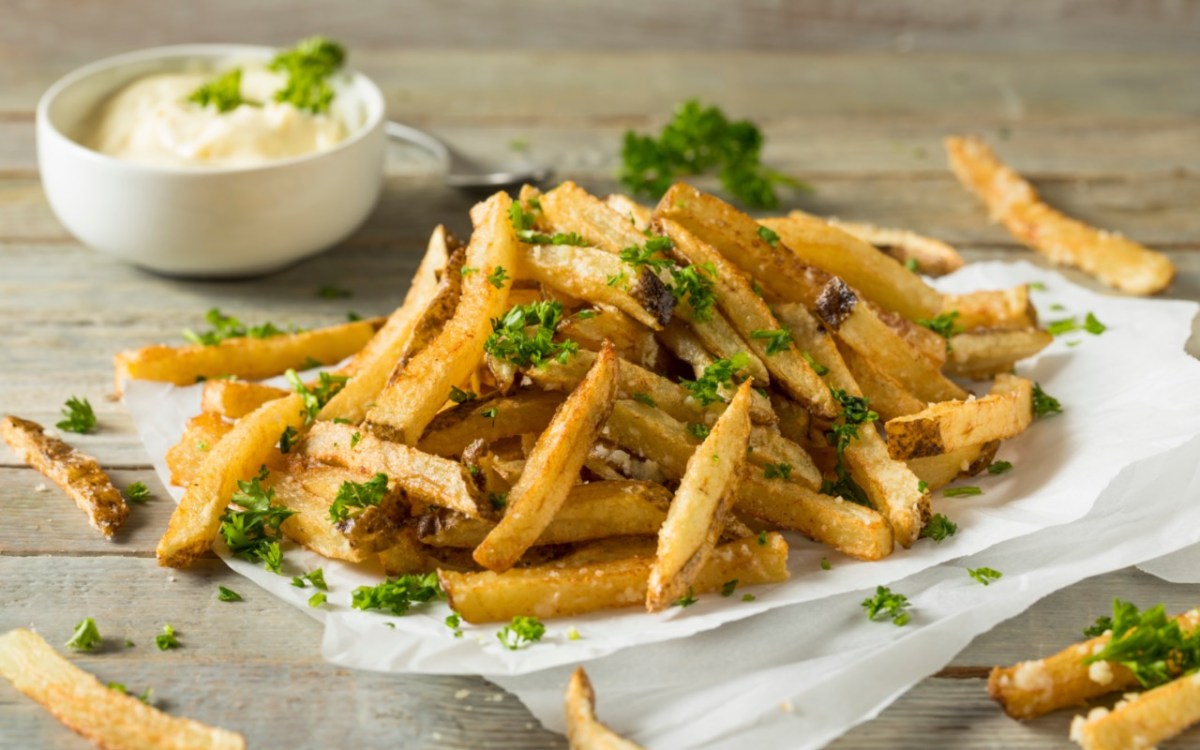 Eine Portion Trüffelpommes mit Petersilie und einer Schale mit Dip.