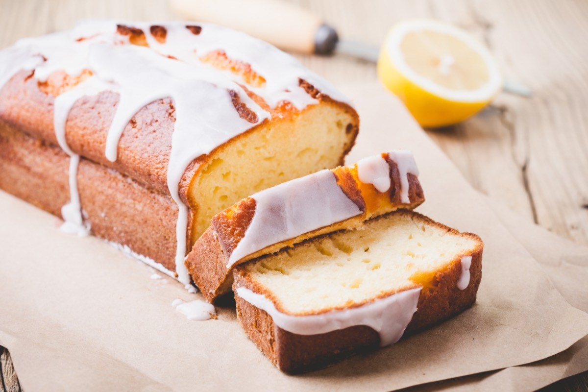 Ein Zitronen-Mascarpone-Kuchen, der an einer Seite schon in Stücke geschnitten wurde. Im Hintergrund liegt eine halbe Zitrone.