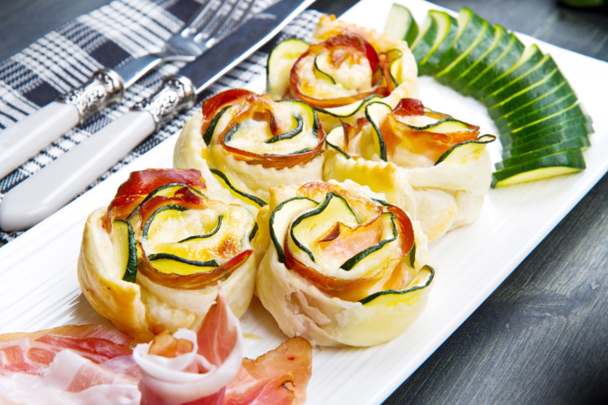 Fünf Zucchini-Blätterteig-Rosen auf einer eckigen Servierplatte.