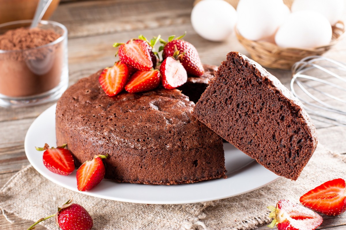 3-Zutaten-Schokokuchen dekoriert mit Erdbeeren, aus dem ein Stück herausguckt.