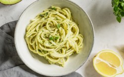 Ein Teller Avocado-Basilikum-Pasta in der Draufsicht. Drumherum liegen frische Zutaten.