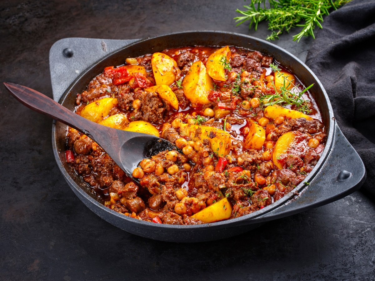 Bauerntopf mit Hackfleisch, Kartoffeln, Paprika und mehr GemÃ¼se in einer tiefen Pfanne, darin ein HolzlÃ¶ffel, Nahaufnahme.