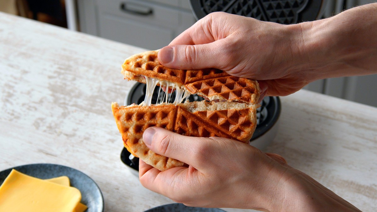 Gefülltes Brötchen im Waffeleisen wird von zwei Händen auseinander gebrochen.