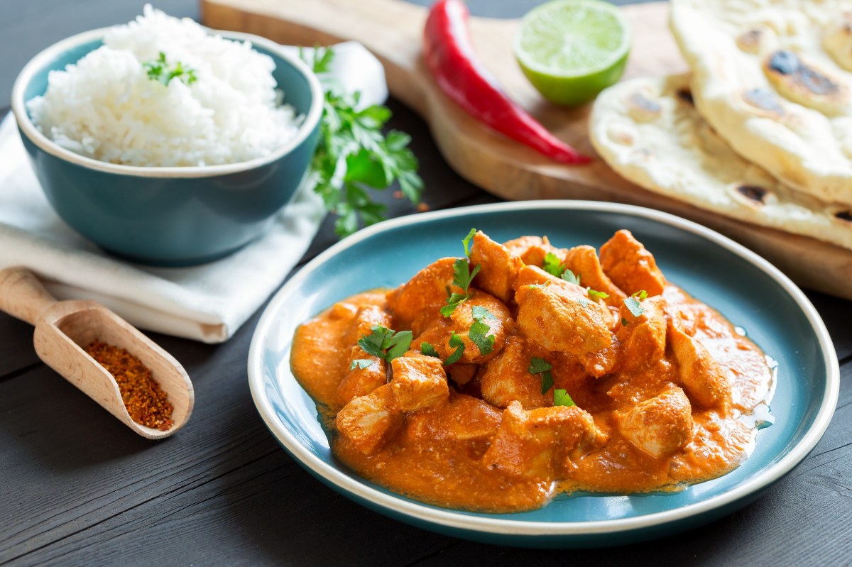 Butter Chicken auf einem hellblauen Teller. Im Hintergrund unscharf Reis und Naan.