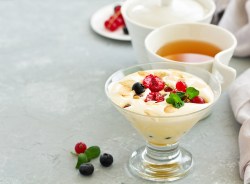 Ein Glas Eierlikör-Mousse garniert mit Beeren und Mandeln, dahinter eine Tasse Tee.