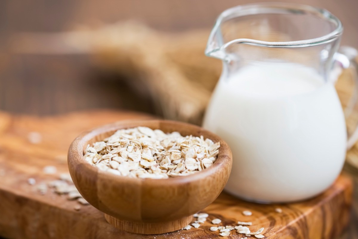Ist Hafermilch gesund: Eine Glaskaraffe mit Hafermilch- daneben eine Schüssel Haferflocken.