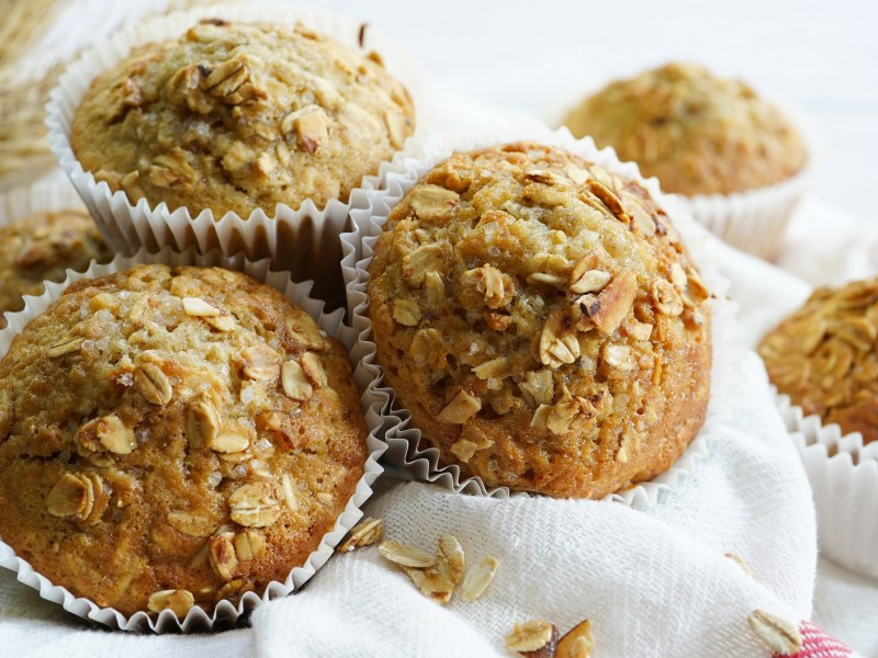 Mehrere Müsli-Muffins in weißen Muffinförmchen aus Papier auf einem weißen Tuch.