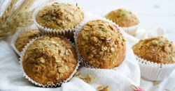 Mehrere Müsli-Muffins in weißen Muffinförmchen aus Papier auf einem weißen Tuch.